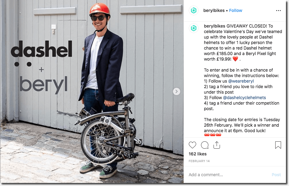 Screenshot of an Instagram giveaway by a cycling brand. The main image shows a casually-dressed young man, wearing a red helmet and sunglasses, and carrying a folding bike in one hand. The competition invites people to follow, comment, and tag for the chance to win a helmet and lights.