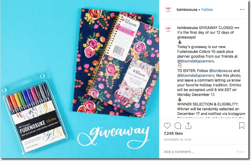 A Christmas Instagram giveaway from Tombow USA. Day 12: a pack of color pens and some planners from a brand associated with Tombow, set against a blue background and the word "giveaway" in white calligraphed text. Users have to follow both brands, like the photo, and comment with their favorite holiday tradition.